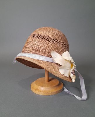 chapeau de paille beige orné d'un ruban blanc et d'une fleur, posé sur un support en bois