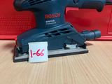 une ponceuse orbitale Bosch posée sur une table, à côté d'une boîte rouge