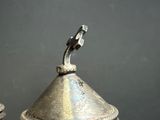 a silver vase with a bird on top of it