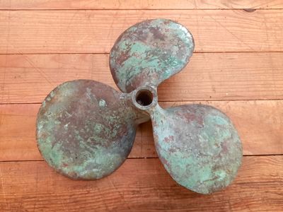 a bronze propeller sitting on a wooden floor