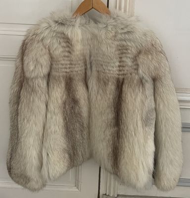 une veste en fourrure blanche suspendue à un cintre en bois devant une porte