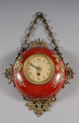 a red clock hanging from a chain on a wall