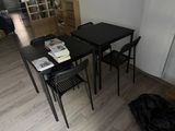a black table with four chairs and a bookcase in the corner