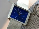 a silver watch with a blue face sitting on a leather strap