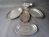 four silver plates and a creamer sitting on a table