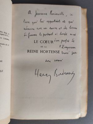 un livre ouvert, sur lequel est inscrit un poème manuscrit, posé sur une table