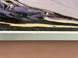peinture abstraite violette et noire sur un cadre blanc posé sur une surface marron