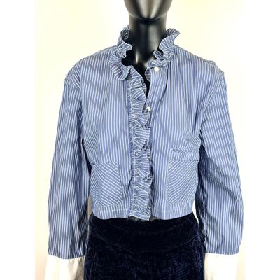 La chemise est rayée de bleu et de blanc et possède un col à volants.