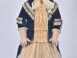 une poupée ancienne représentant une femme vêtue d'une robe bleue et d'un chapeau