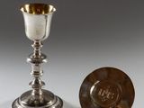 une coupe et une assiette en argent posées sur une surface blanche avec un fond gris