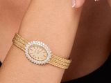 La femme porte au poignet un bracelet en or avec une montre sertie de diamants.