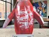 une statue de pingouin rouge posée sur une table devant une fenêtre
