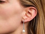 the woman is wearing a pair of earrings with pearls hanging from them