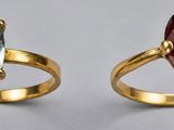 two rings with different colored stones are shown on a table