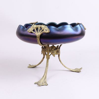 un bol violet posé sur un socle doré, sur fond blanc