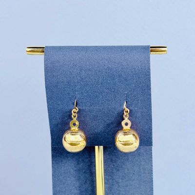 des boucles d'oreilles posées sur un présentoir recouvert d'un tissu bleu, surmonté d'une boule dorée