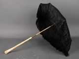 un vieux parapluie noir avec un manche en bois posé sur une surface grise