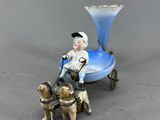 une figurine représentant un garçon sur une petite charrette, accompagné de deux chiens