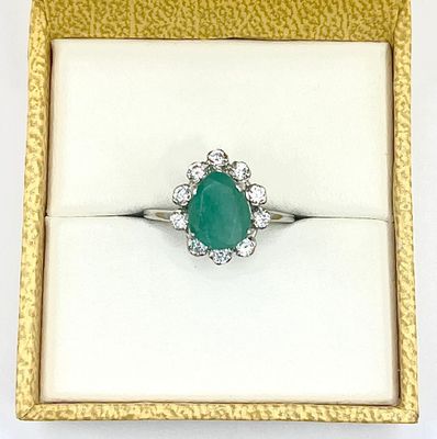 an emerald and diamond ring in a gold box on a white surface
