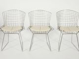three chrome wire chairs with beige seat padding against a white background