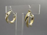 Boucles d'oreilles créoles bicolores or et argent, présentées sur un support en acrylique transparent
