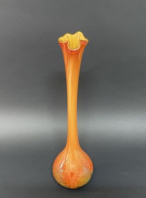 un vase orange posé sur une table noire, près d'un mur gris