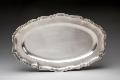 a silver plate with a scalloped edge on a gray surface