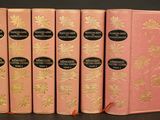quatre livres roses ornés de motifs à la feuille d'or, posés sur une table