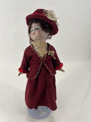 une petite poupée qui porte une robe rouge et un chapeau