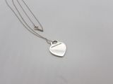 a silver heart shaped pendant with a chain on a white surface