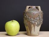 a green apple next to a brown vase on a table