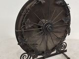 roue en fer forgé posée sur un socle, sur fond blanc avec un mur blanc