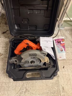 une boîte à outils ouverte posée par terre, contenant une scie circulaire