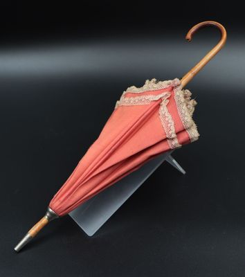 a pink umbrella with lace on it sitting on a stand