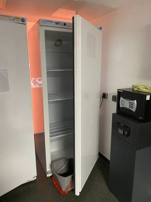 an open refrigerator in the corner of a room next to a trash can