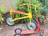 un tricycle rouge et jaune à côté d'un buisson vert