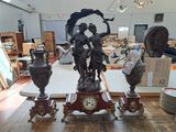 trois statues posées sur une table surmontée d'une horloge