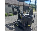 the back end of a small excavator parked in a gravel lot