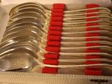 a lot of silver spoons in a box with red handles