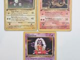 Trois cartes Pokémon sont posées sur une table avec un fond blanc.