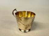 an antique silver cup with a handle on a white surface