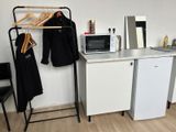 a small kitchen with a microwave, refrigerator, and clothes rack