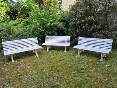 three white benches sitting in the grass near some bushes