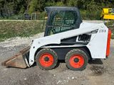 a picture of a small ski - loader parked in a gravel lot