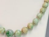 a close up of a necklace with green beads on a white mannequin