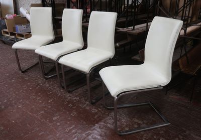 quatre chaises de salle à manger en cuir blanc disposées dans une pièce à côté d'un escalier