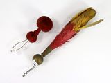 a red and yellow feather and two red balls on a white surface