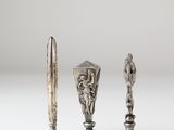 a set of three silver vases and a knife on a white surface
