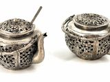 two silver teapots sitting next to each other on a white surface