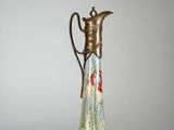 un vase en verre muni d'une poignée en métal posé sur une surface blanche